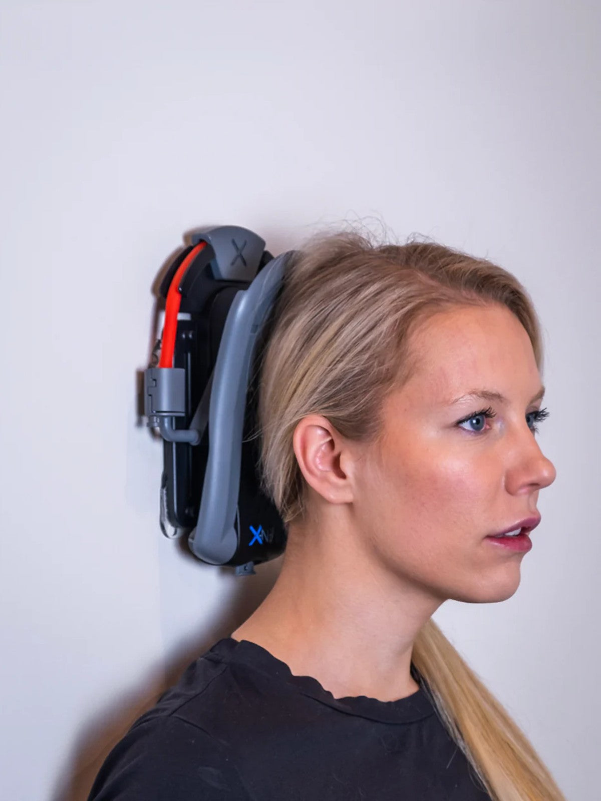 Woman demonstrating proper use of the XtreemNek neck strengthening device against a wall, performing the Chin Tuck Exercise for improved posture and neck pain relief-2