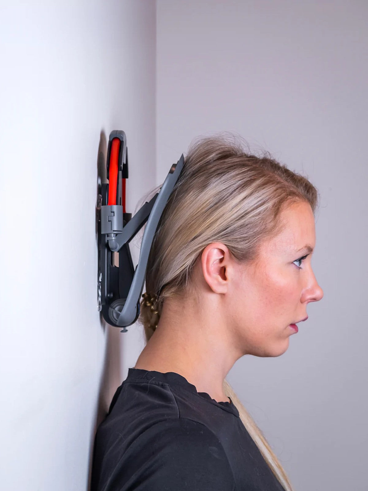 Woman demonstrating proper use of the XtreemNek neck strengthening device against a wall, performing the Chin Tuck Exercise for improved posture and neck pain relief.